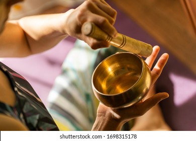 Top View Of A Young Yogin Woman Holding A Tibetan Bowl And A Stick In The Beautiful And Gentle Light Of Morning During A Yoga Session, Creating A Meditative State Through Music.