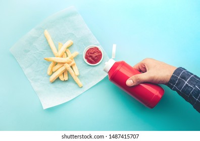 Top view of youngman squeezing a bottle sauce ( ketchup ) for dipping with french fried on blue color background.Fast food and healthy concepts ideas
