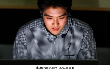 From top view zoom focus to asian man face one of helpdesk support team wearing headphone sitting and look at monitor with look feel happy with smiling.