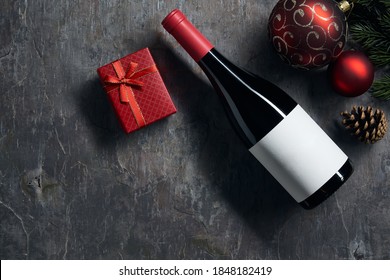 Top Viiew Of Bottle Of Red Wine With Blank White Label With Christmas Decorations And Gift Box On Dark Background. Wine Bottle Mockup.