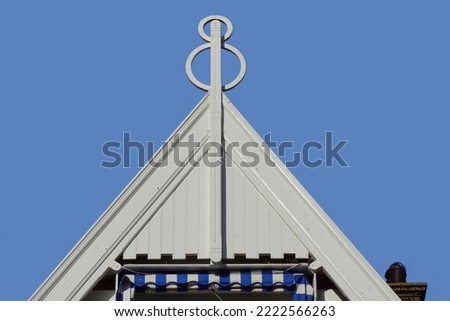 Top of a white wooden facade with a finial or hip knob as a decorative feature. Roof spire of a Dutch house. Blue sky. Canopy top.                               