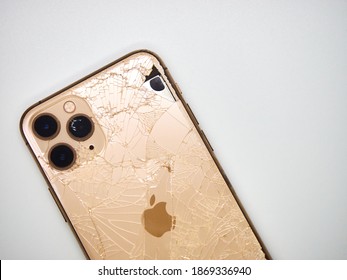 Top wiev the back of gold smartphone iPhone 11 Pro with a broken glass and a damaged curved body close-up isolated on white background