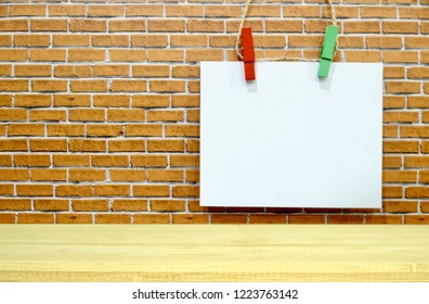 Top Wood Table With White Paper Note Hanging On Orange Brick Background. Colorful Wood Clips. Free Space For Any Text Design. Can Be Use For Advertising, Banner. Montage For Display Product.