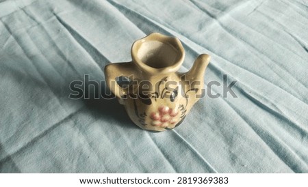 Top-angle view of a painted miniature ceramic teapot featuring floral motifs on light blue textured fabric background.