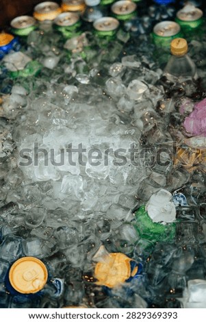 Top-down close-up of assorted beverage cans surrounded by melting ice cubes in a cooler, emphasizing cold refreshment at an outdoor event