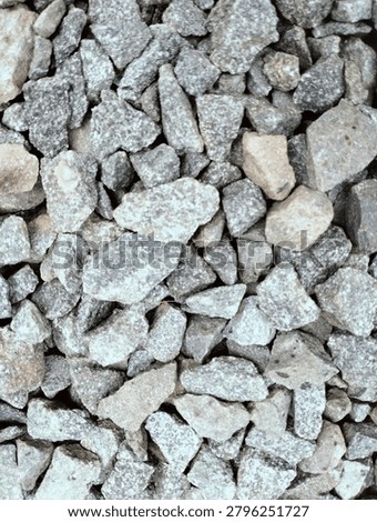 Top-down close-up shot of angular crushed stone aggregate, featuring mixed shades of gray, off-white, and light brown. Natural rough texture of granite gravel, commonly used in construction, road base, concrete mixing, landscaping, and outdoor paving. Detailed surface pattern with varying stone sizes, suitable as a background or material reference.