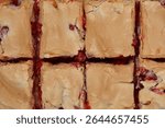 
A top-down close-up shot shows a freshly baked currant and meringue cake cut into squares, revealing a vibrant red fruit filling underneath a golden-brown baked meringue topping