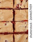 
A top-down close-up shot shows a freshly baked currant and meringue cake cut into squares, revealing a vibrant red fruit filling underneath a golden-brown baked meringue topping