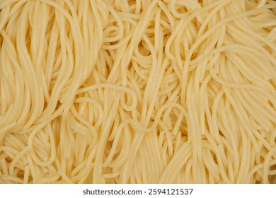 A top-down, close-up shot of a tangled mass of cooked spaghetti, displaying their soft, creamy yellow color and intertwined texture