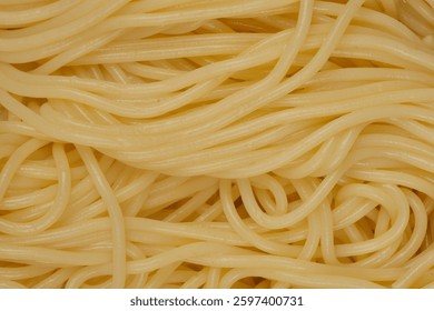 A top-down, close-up shot of a tangled mass of cooked spaghetti, displaying their soft, creamy yellow color and intertwined texture