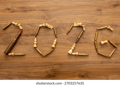 Top-down composition shows bullets and chess pieces forming “2026” on wood with a nearby magazine; the image reads as a visual forecast combining calendar reference and staged military symbolism.