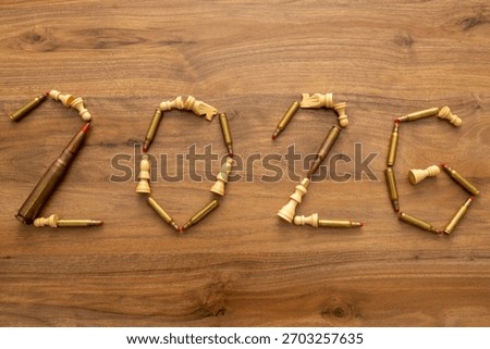Top-down composition shows bullets and chess pieces forming “2026” on wood with a nearby magazine; the image reads as a visual forecast combining calendar reference and staged military symbolism.