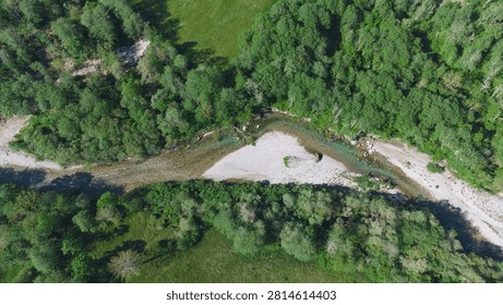 Top-down drone perspective of a shallow mountain river curving around a white gravel sandbar, flanked by dense green forest and meadow.