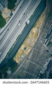Top-down drone view of multilane highway with moving vehicles, railway yard with numerous tracks, and a narrow canal running between them. Complexity of modern transportation networks