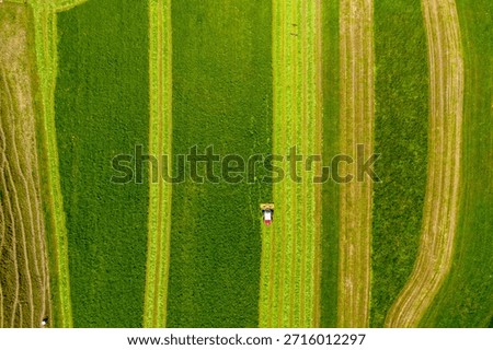 Top-down drone view of tractor mowing striped green fields near Bantiger, Bern, Switzerland