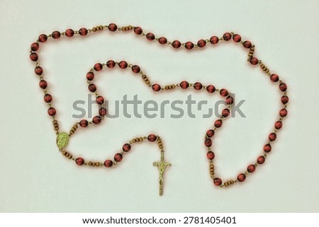 Top-down flat lay view of a traditional catholic rosary with brown reddish wooden beads gold metal chain connections small oval center medal and a crucifix cross pendant on a white surface area