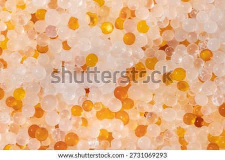 A top-down macro shot captures a dense mix of tiny, translucent jelly granules in shades of translucent white and amber orange.