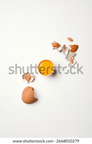 Top-down minimal composition of three raw yolks in half shells arranged as a triangle on a bright white background.