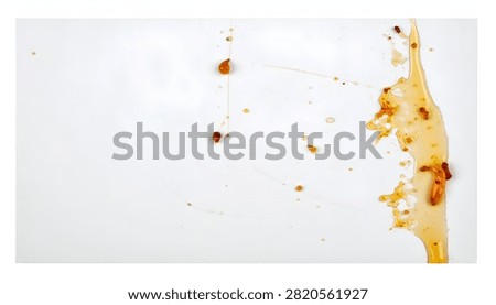 A top-down perspective captures a viscous spill of golden honey on a bright white background with distinct droplets and scattered small particles