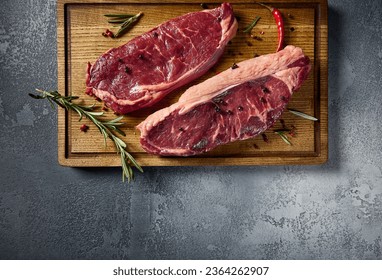 A top-down perspective capturing raw striploin and New York steaks on a wooden board. The untouched beef reveals its marbled texture, set against a simple gray backdrop. - Shutterstock ID 2364262907