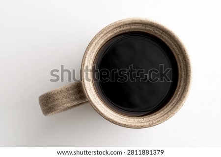 A top-down perspective showcases a simple, handcrafted wooden mug brimming with rich, dark coffee, set against a clean white background.