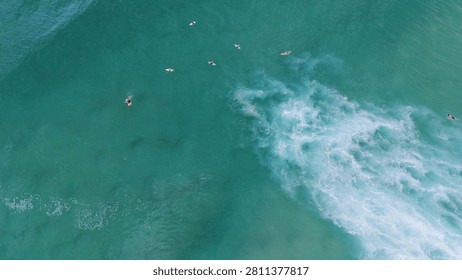 Top-down perspective of surfers floating in turquoise ocean water near breaking white foam waves.