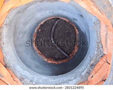 Top-down perspective view looking deep inside a newly constructed precast concrete water well shaft with a dirt bottom and a metal pipe.