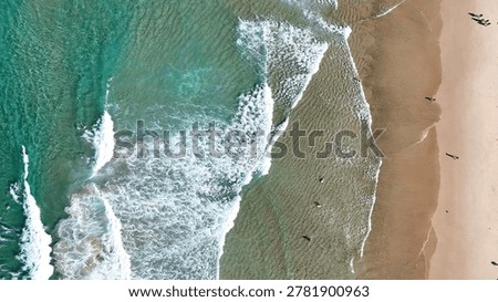 Top-down perspective of white ocean foam washing over sandy shores with distant beachgoers.