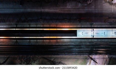 A top-down shot directly over a empty railroad train station at night, with the glow of the street lights and the station platform lights.