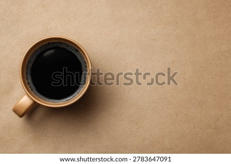 A top-down shot showcases a rustic ceramic mug brimming with rich, dark coffee, set against a textured brown background.