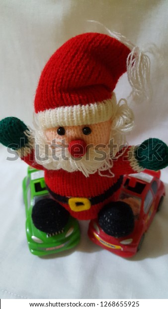 A top-down shot of a\
stuffed toy, a replica of Santa Clause rolling on two toy model\
racing cars. One car is red the other green. Santa is decked in his\
Santa suit. 