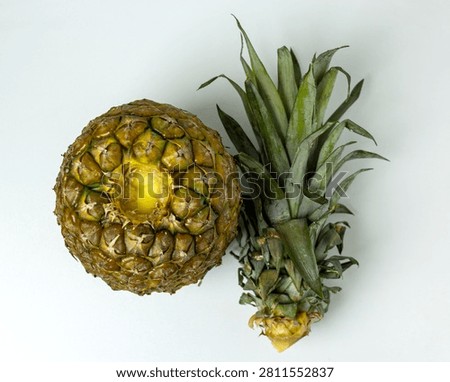 Top-down studio shot of a fresh ripe pineapple with its green crown neatly separated and placed beside the fruit, highlighting the textured rind and bright core on a clean white background. Great for food, wellness and tropical concepts