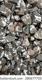 Top-down texture of angular crushed grey stone splattered with white and a few red paint drops, filling the frame as a rough industrial background. The sharp gravel fragments and contrasting paint marks create a gritty abstract pattern with natural stone detail. Ideal for construction, landscaping, grunge and design backgrounds, overlays and texture use with plenty of surface detail
