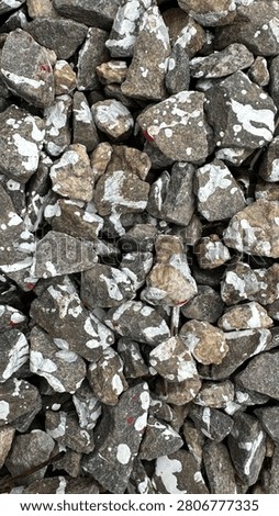 Top-down texture of angular crushed grey stone splattered with white and a few red paint drops, filling the frame as a rough industrial background. The sharp gravel fragments and contrasting paint marks create a gritty abstract pattern with natural stone detail. Ideal for construction, landscaping, grunge and design backgrounds, overlays and texture use with plenty of surface detail