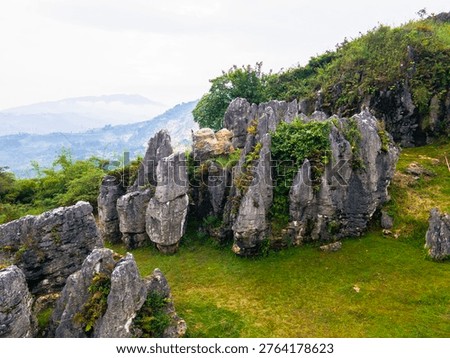 Top-down view of ancient rock formations scattered across green fields. Unique geological karst landscape with weathered limestone boulders, at Stone Garden, Padalarang, Bandung, Indonesia.