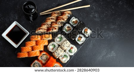 Top-down view of an assorted sushi platter with salmon, eel, tobiko and black caviar rolls, soy sauce and chopsticks on a dark slate board.