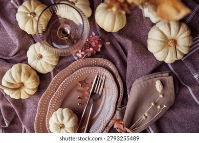 A top-down view of an autumn-themed table featuring soft pink plates, white pumpkins, and warm textures. Perfect for seasonal invitations, fall decor ideas, and Thanksgiving celebrations