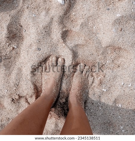 Top-down view of a barefoot woman standing on sandy beach, a tranquil moment embracing the soothing touch of nature.