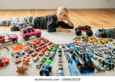 Top-down view of a boy lying on the floor surrounded by a vast, colorful collection of toy cars neatly arranged in rows childhood hobby and play