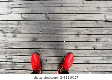 A top-down view of bright red sneakers standing on a weathered wooden deck, showcasing casual footwear and rustic textures. - Powered by Shutterstock