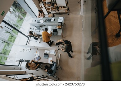 Top-down view of a bustling open-plan office with diverse professionals collaborating at desks and in casual seating areas, exemplifying teamwork in a modern workplace setting. - Powered by Shutterstock