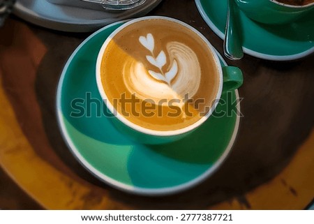 Top-down view of a caffe latte with elegant tulip and heart latte art in a teal ceramic cup on a wooden table.