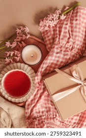 A top-down view captures a serene spring morning scene featuring delicate pink hyacinths, a burning candle, and a beautifully wrapped gift box on a gingham cloth