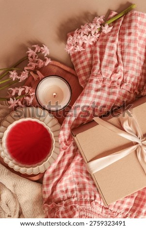 A top-down view captures a serene spring morning scene featuring delicate pink hyacinths, a burning candle, and a beautifully wrapped gift box on a gingham cloth