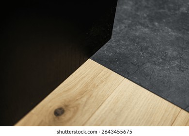 Top-down view of a clean contrast between matte black stone tile and warm wood plank flooring, highlighting texture, tone, and minimalist interior design