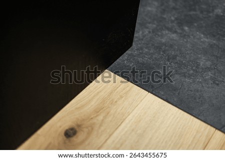 Top-down view of a clean contrast between matte black stone tile and warm wood plank flooring, highlighting texture, tone, and minimalist interior design