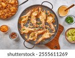 Top-down view of a delicious butterfly shrimp dish served with creamy butter sauce, garnished with fresh parsley. Accompanied by sides of seasoned rice, lime slices, and sauces on a rustic background