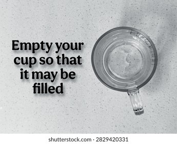 Top-down view of empty clear glass mug on speckled surface with inspirational quote about learning, growth, and open-mindedness.