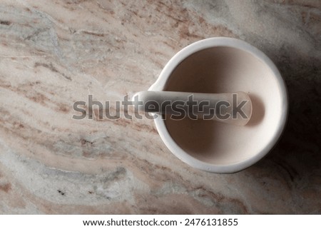 Top-down view of an empty white ceramic mortar and pestle, on a marble background.