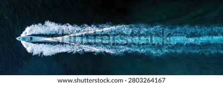 Top-down view of a fast-moving speedboat leaving a prominent white foamy wake on the deep blue ocean.